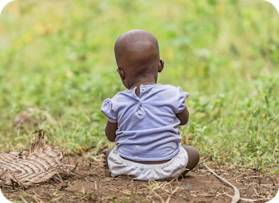 A toddler sat on the grass facing away from the camera