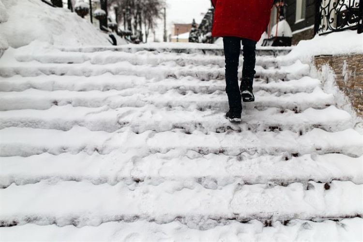 Henkilö kävelee todella vaarallisen näköisiä lumisia portaita ylöspäin