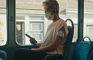Betty zit in de bus met mondmasker en kijkt op haar telefoon