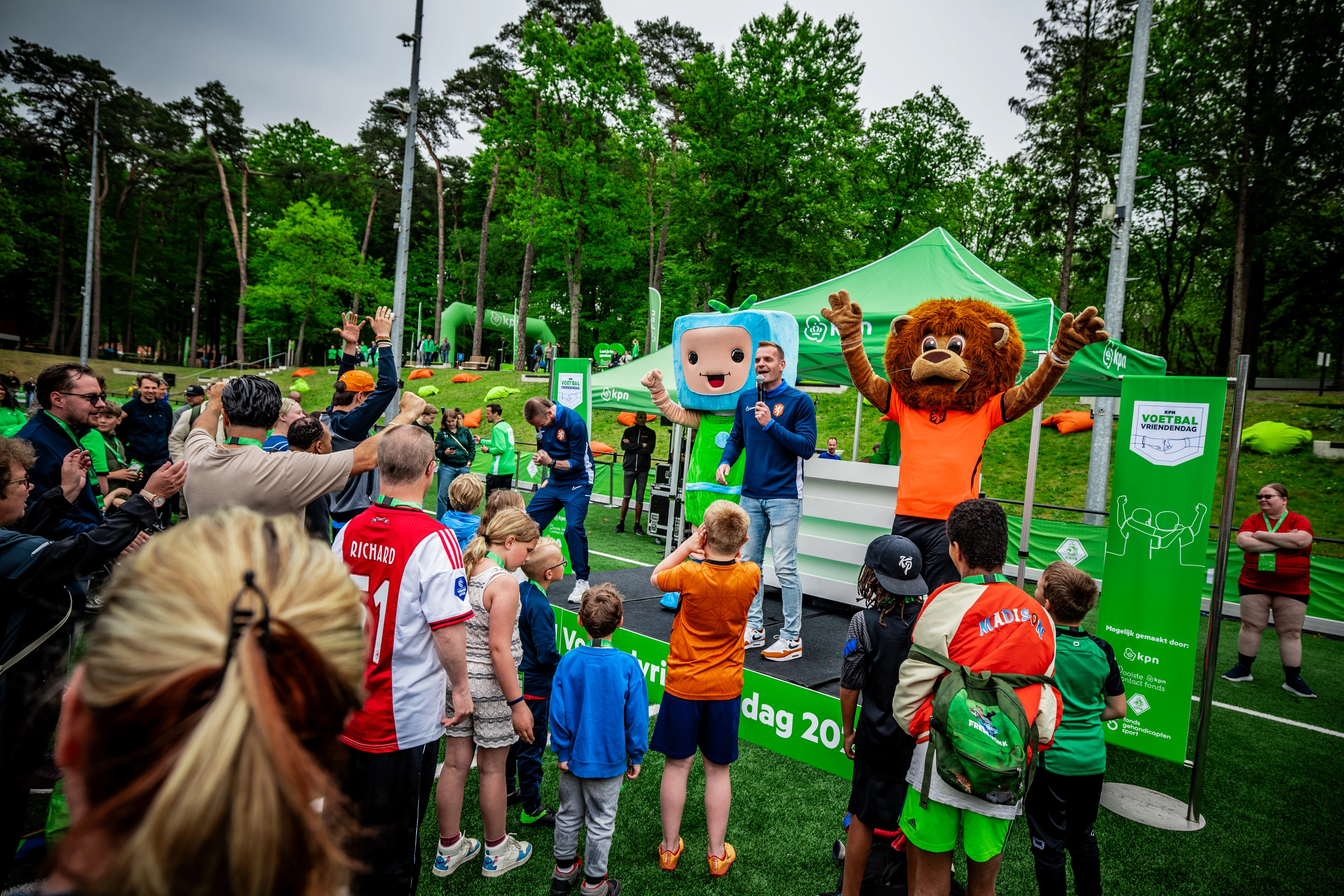 Deelnemers KPN voetbalvriendendag kijken naar podium waar de presentator en de mascotte KNVB op staan