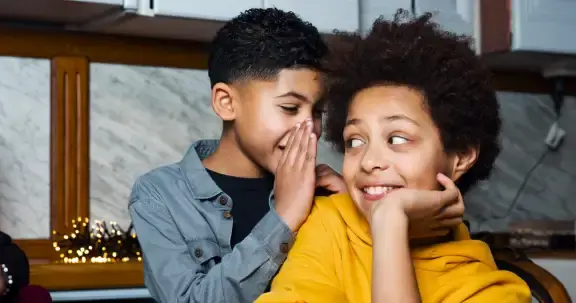 Twee jongens waarbij er ene jongen iets fluistert in het oor van de andere jongen