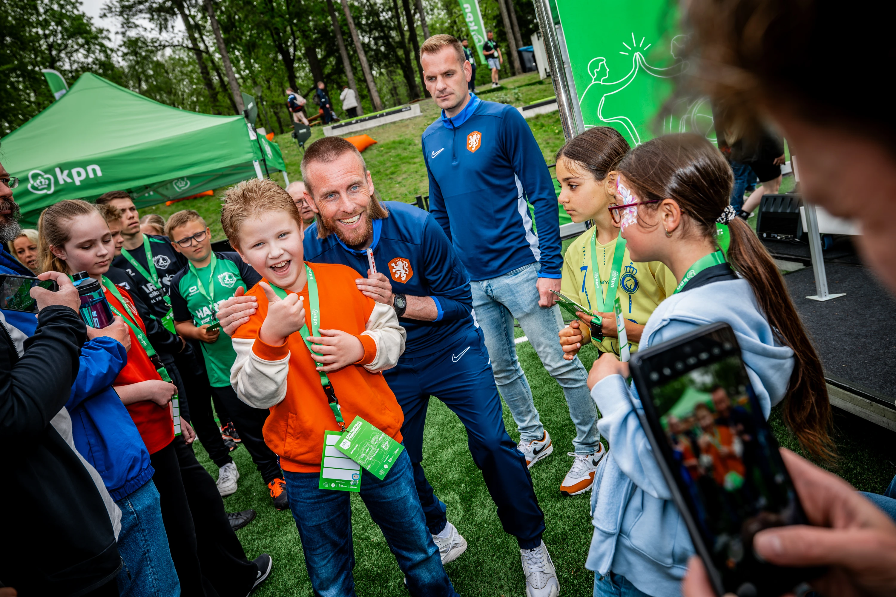 Jongen in oranje jasje poseert samen met Nathan Rutjes voor een foto met andere kinderen er om heen