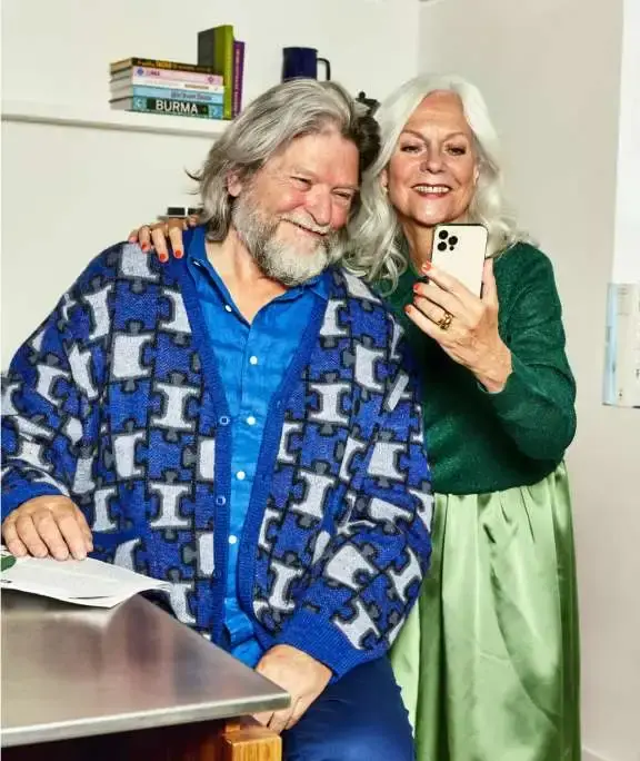 Oudere man en vrouw zittend aan tafel laat de vrouwde man iets zien op telefoon