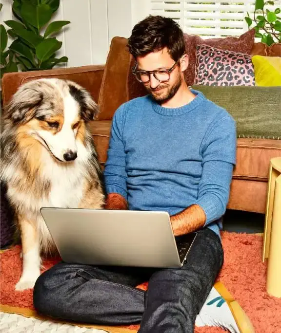 man met hond naast zich zit op de grond en werkt op laptop