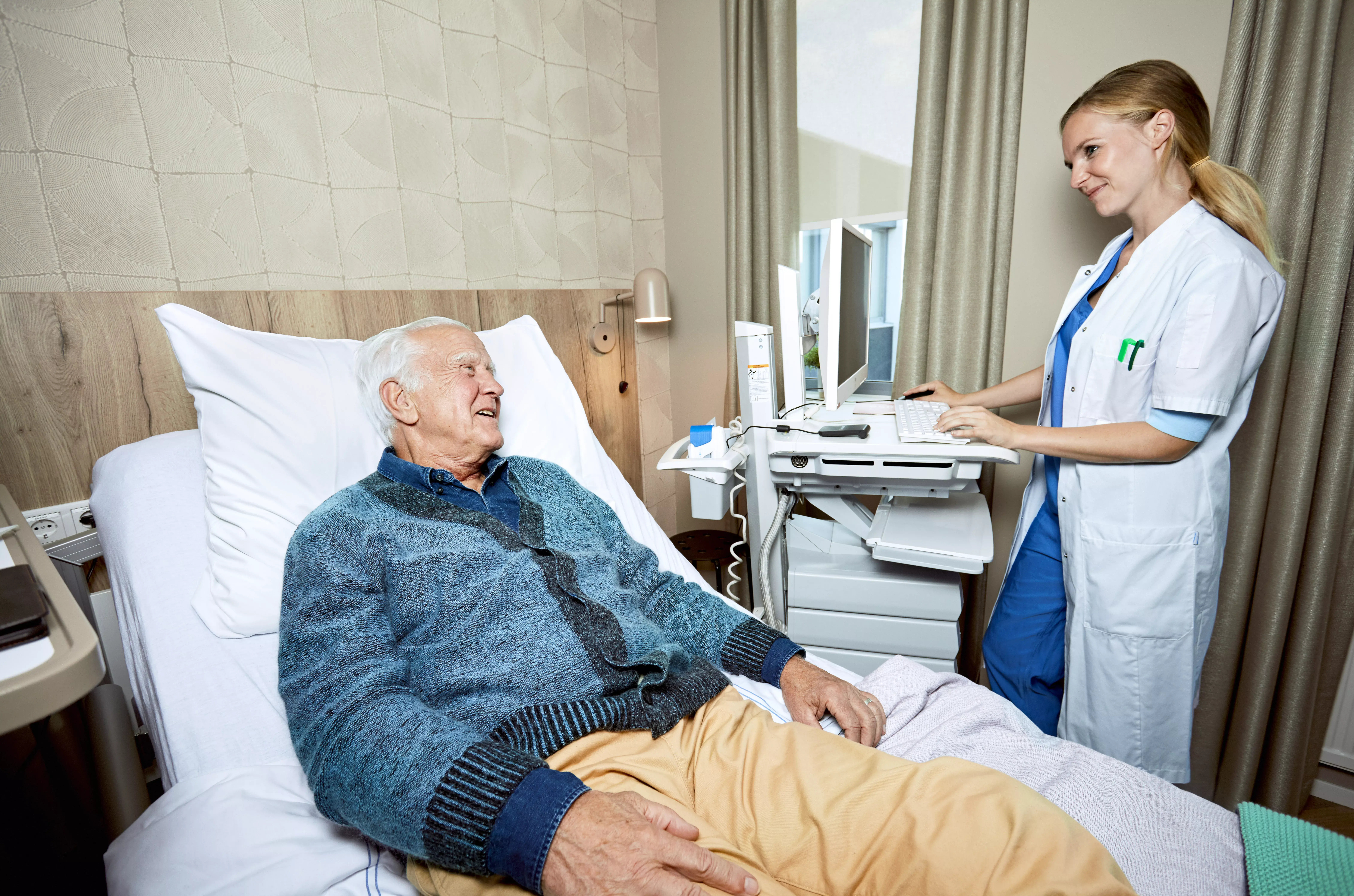 Vrouwelijke arts staat bij oudere man liggend op ziekenhuisbed