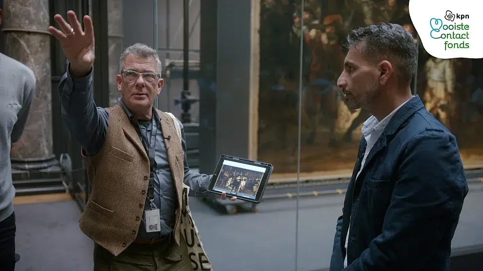 Rondleider in rijksmuseum geeft uitleg over kunstwerk met ipad in de hand