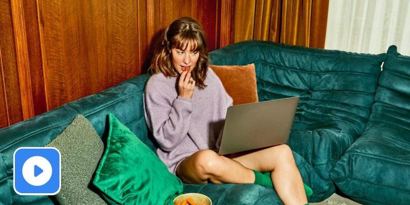 Vrouw eet gezonde snack op de bank met laptop op schoot
