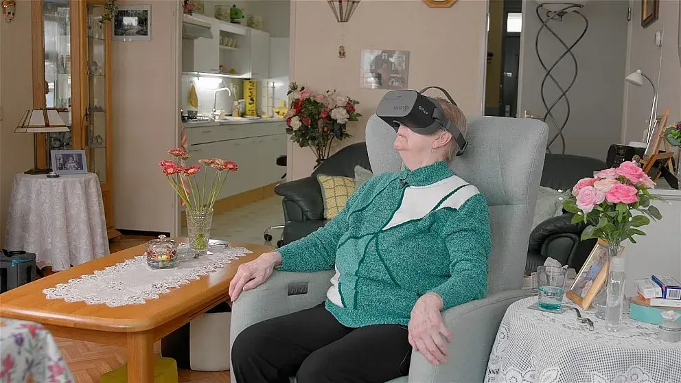 Oudere man in stoel zit met VR-bril op