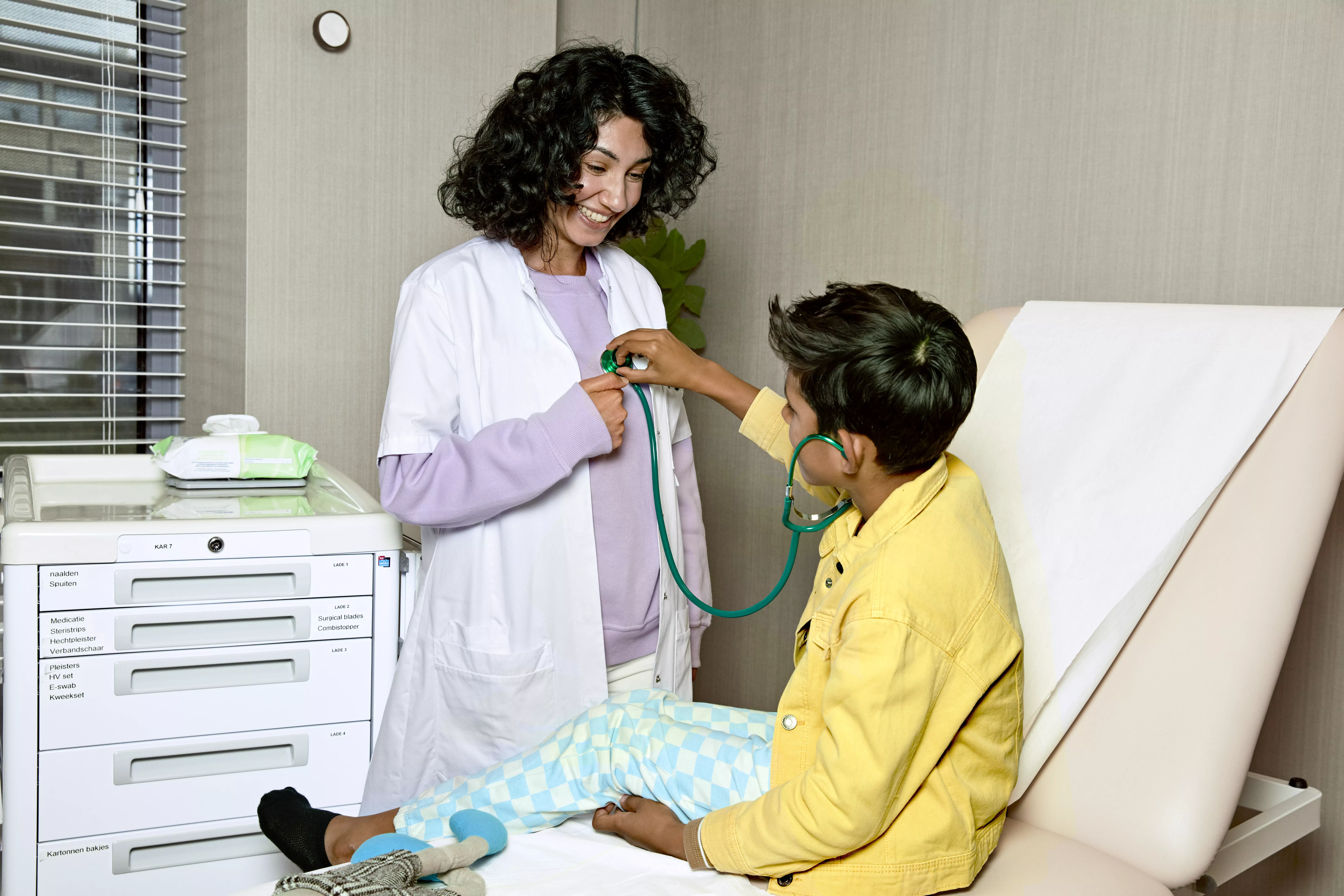 Vrouwelijke arts en jongetje met stethoscoop lachen in een ziekenhuiskamer