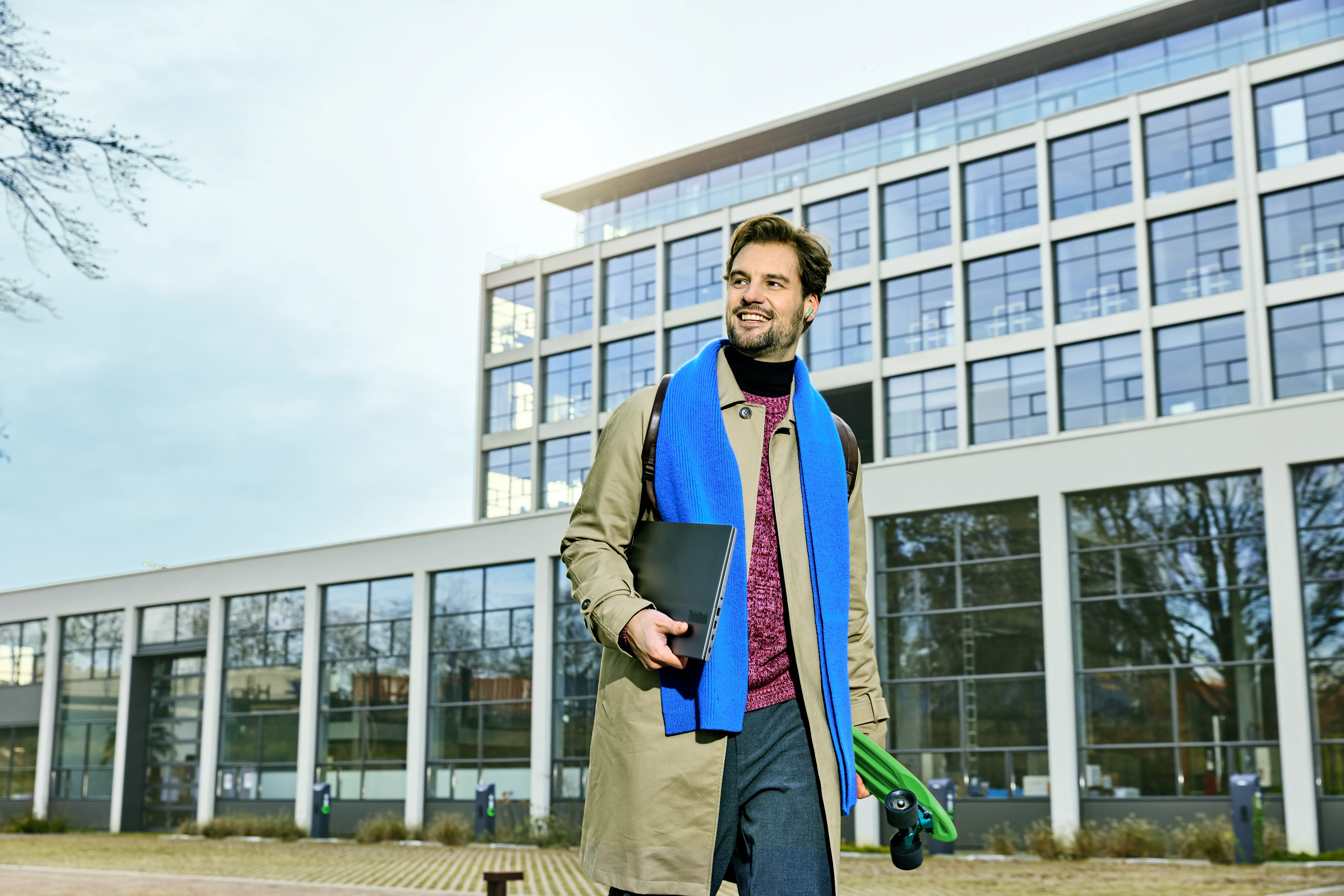 Man met blauwe sjaal loopt met een laptop voor een gebouw