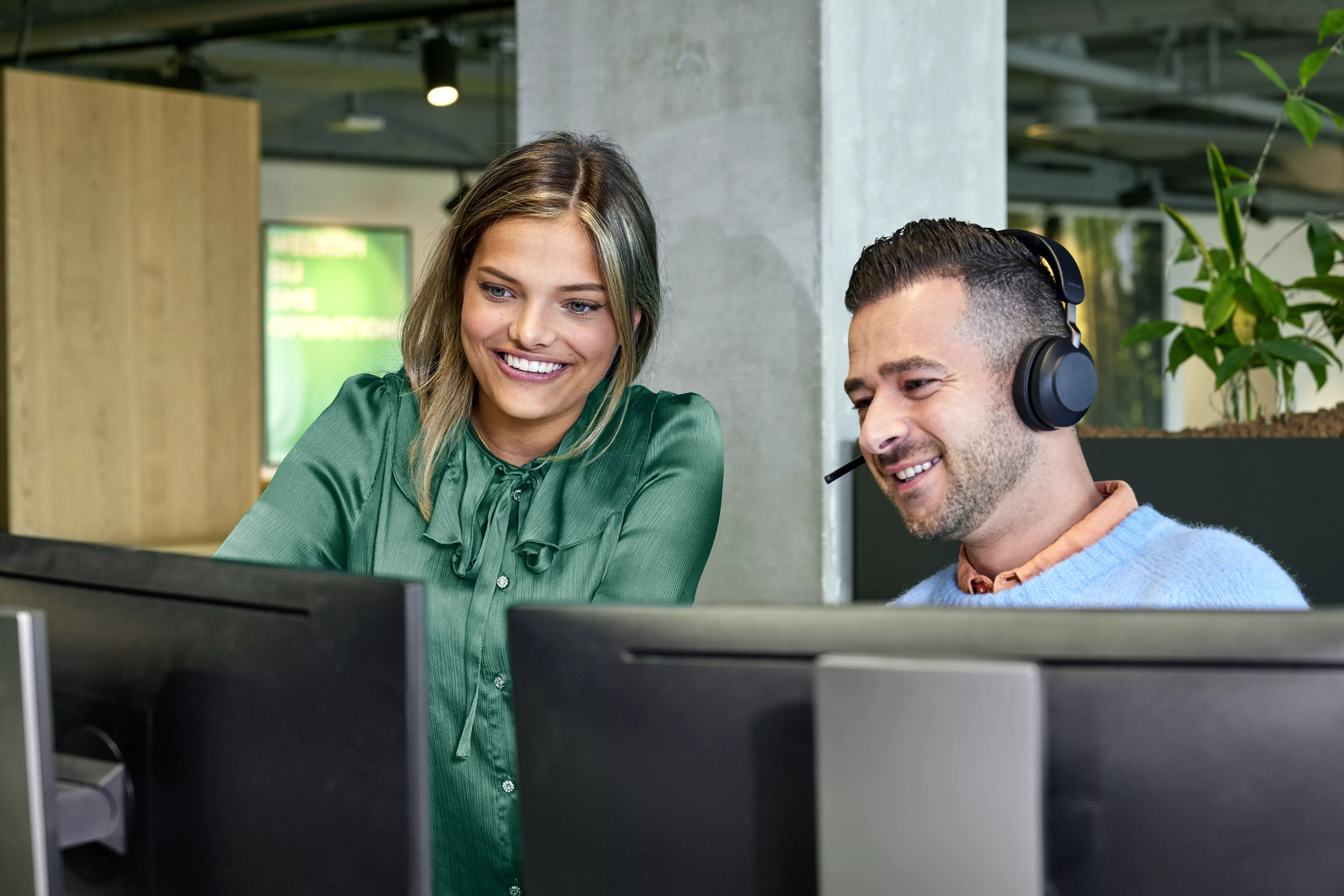 Man en vrouw in callcenter kijken lachend naar een computerscherm