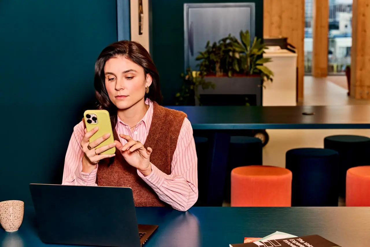 Vrouw op kantoor kijkt aandachtig naar mobiele telefoon