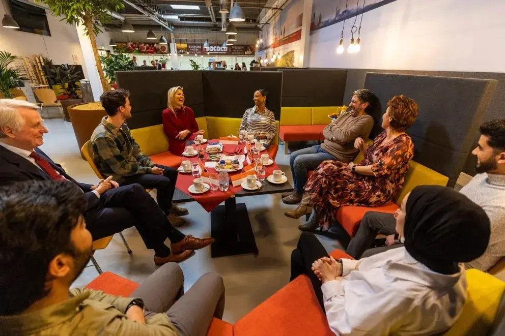 Koninging Maxima op bezoek bij KPN Mooiste Contact Fonds en Oranje Fonds, zittend aan een tafel in gesprek met meerdere mensen