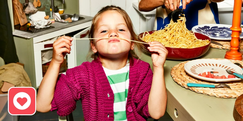 meisje maakt snor van spaghetti aan de eettafel met gezin