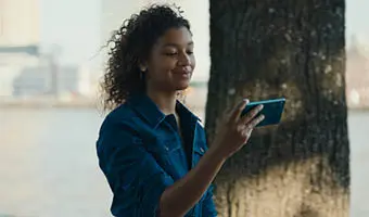 Meisje die op haar iPhone scherm kijkt. Op de achtergrond is een boom te zien en water