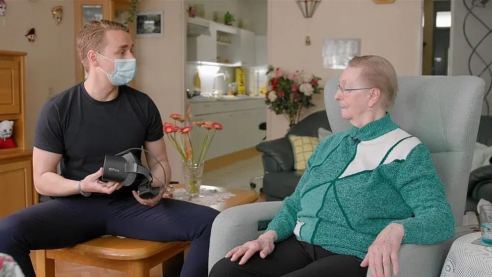 oudere man in stoel krijgt uitleg over de werking van de VR-bril