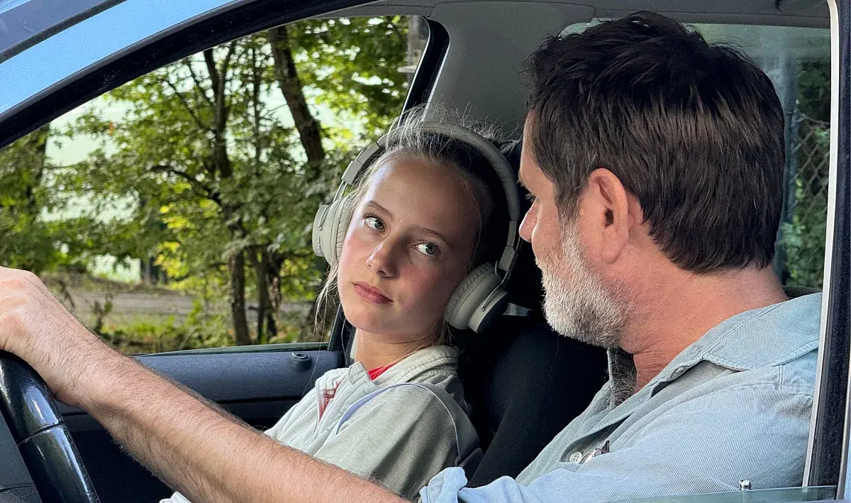 Vader en dochter in auto, kijken elkaar aan, dochter heeft koptelefoon op