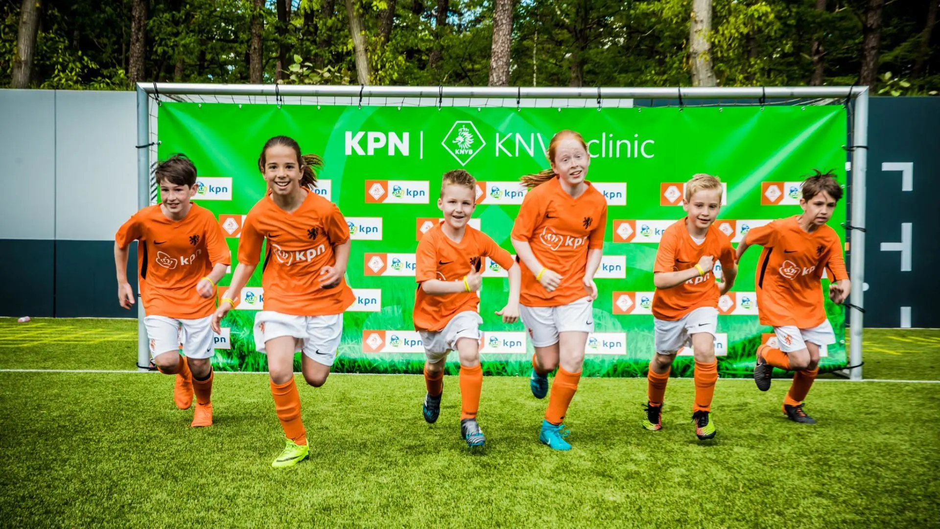 6 kind-voetballers op een rij bij een KPN KNVB clinic. Met oranje voetbalshirts aan met het logo van KPN erop.