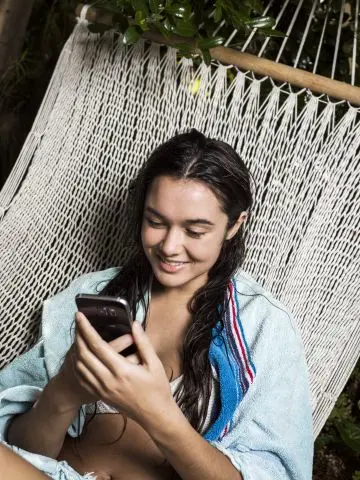 Meisje met donker haar in een hangmat, kijkend naar haar telefoon