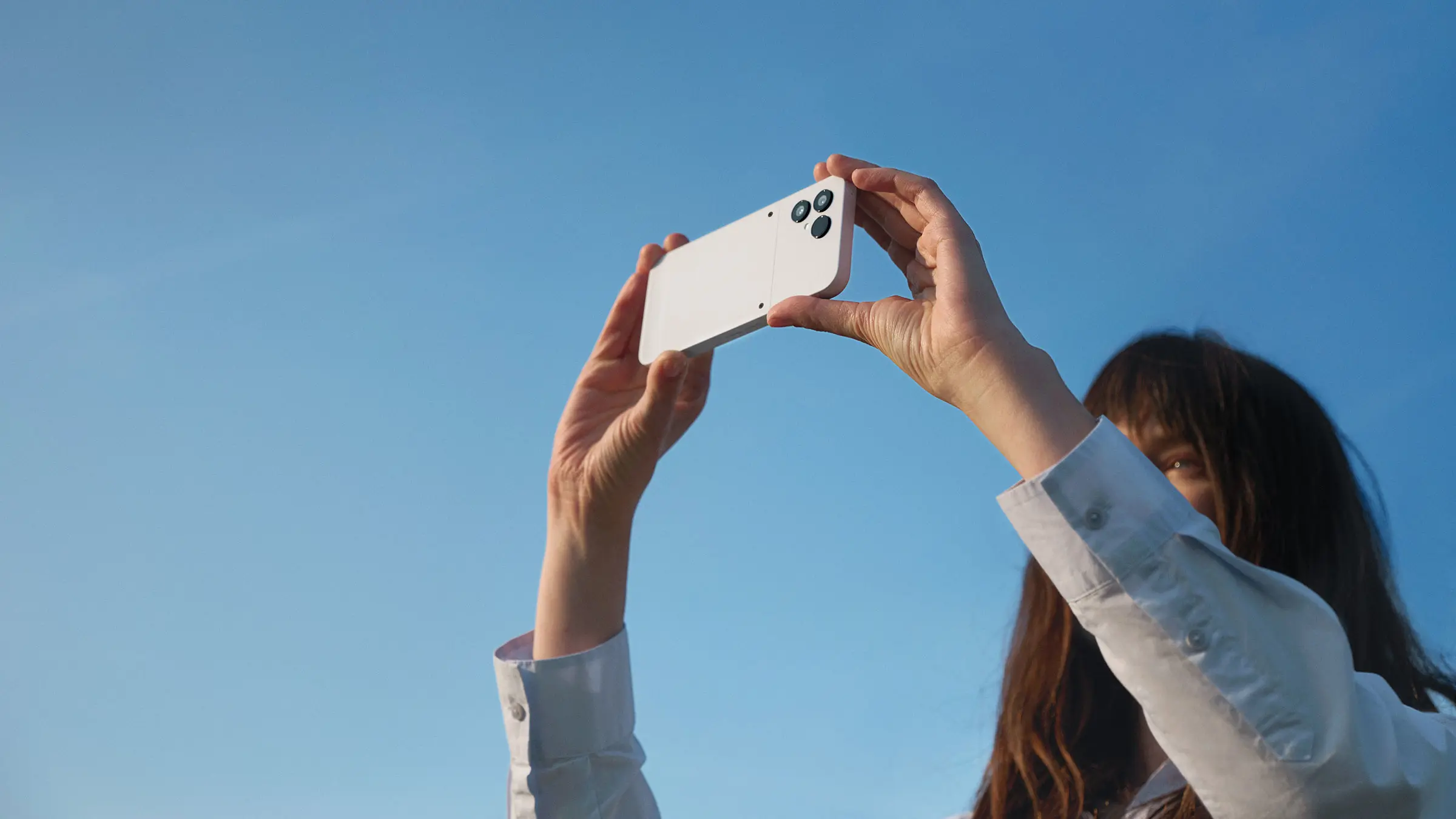 Foto van blauw lucht met vrouw die een telefoon boven haar hoofd houdt