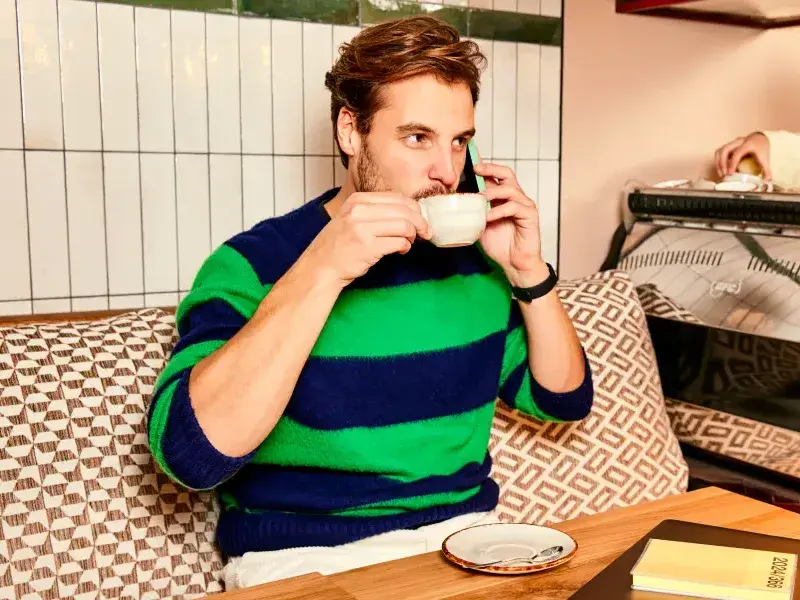 Een man in een koffiezaak drinkt een kop koffie. Hij belt met zijn mobiele telefoon