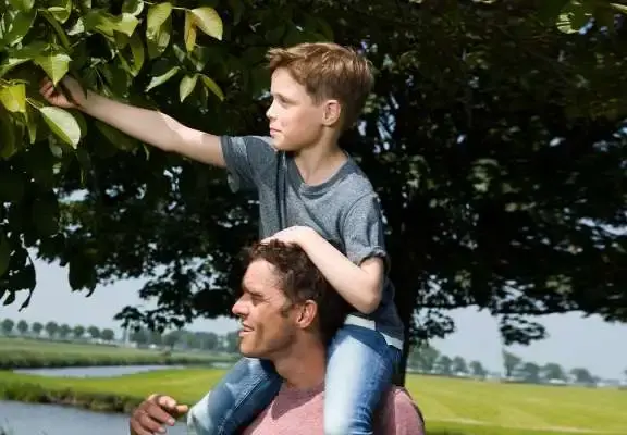 Zoon op de schouders van vader plukt iets uit een boom