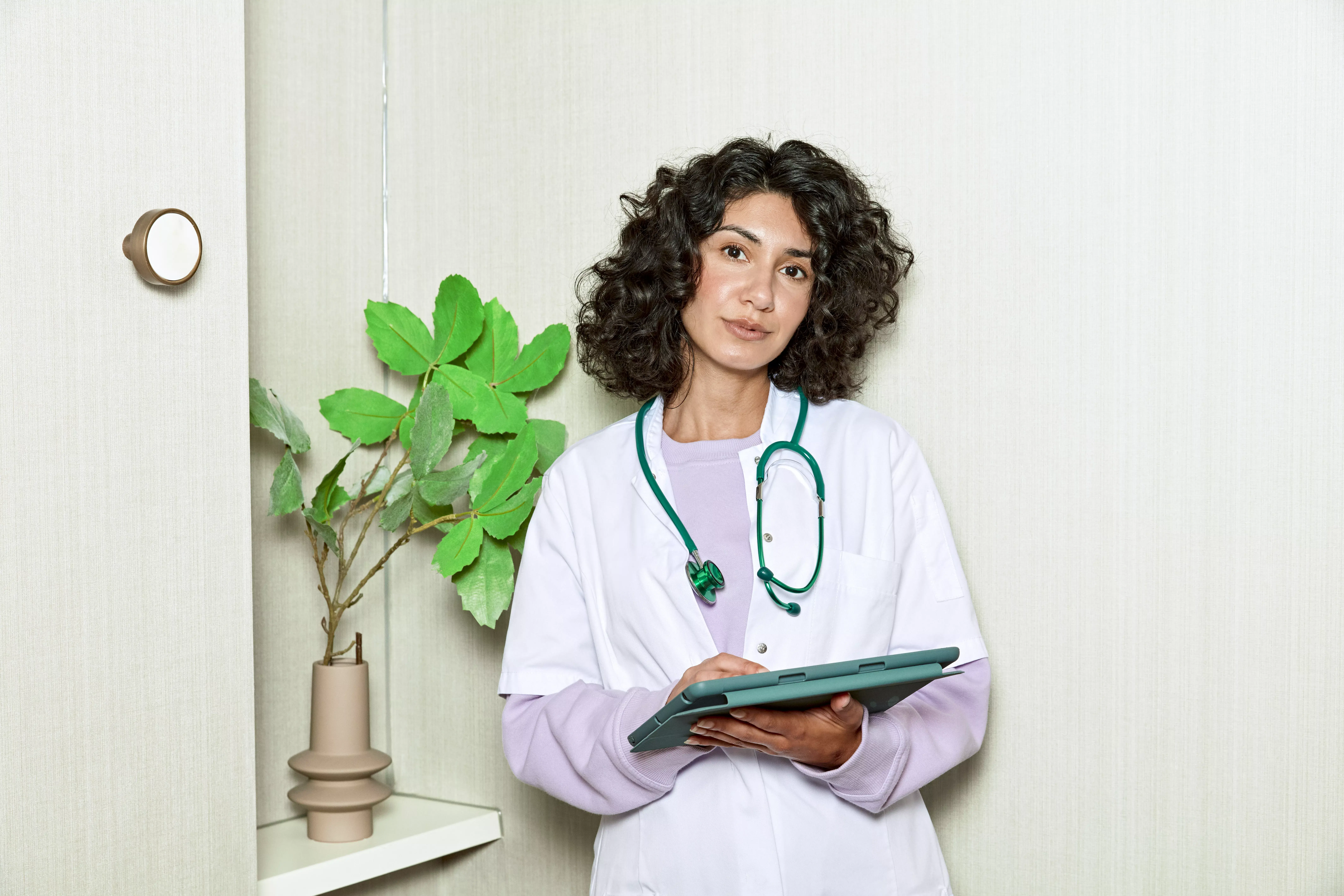 Vrouwelijke dokter staat met tablet naast een plant