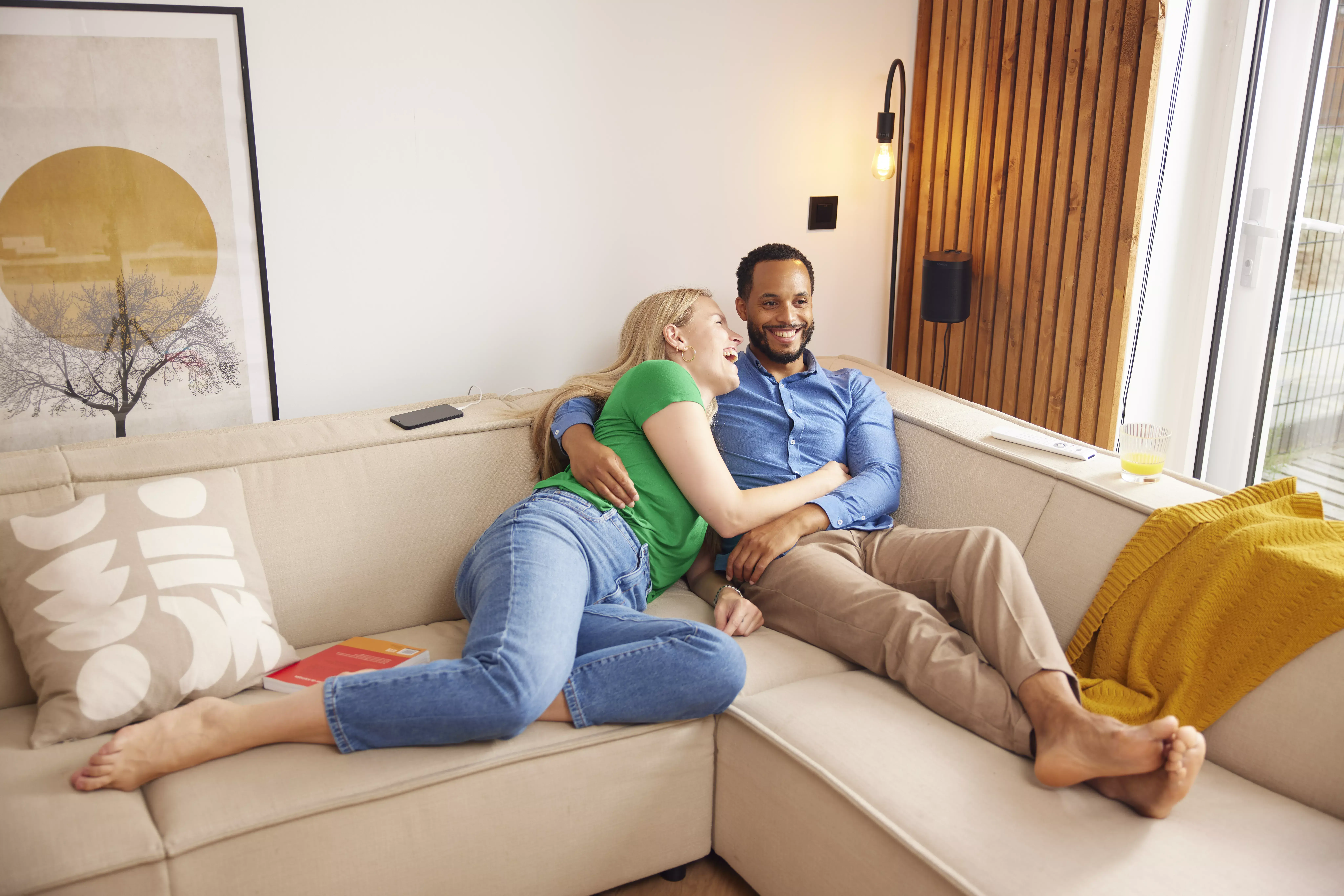 lachende vrouw en man samen liggend op de bank tv aan het kijken