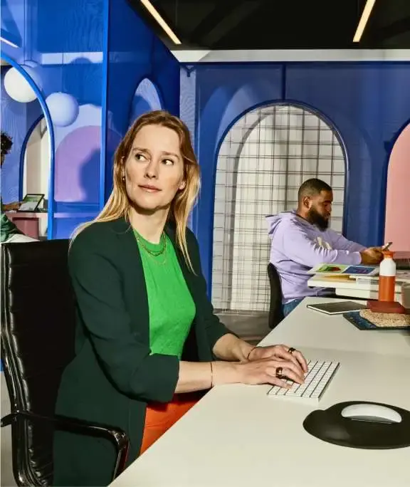 Dame op voorgrond, man op achtergrond zitten achter een bureau