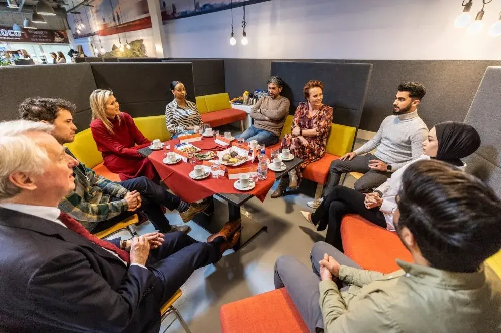 Koninging Maxima op bezoek bij KPN Mooiste Contact Fonds en Oranje Fonds, zittend aan een tafel in gesprek met meerdere mensen