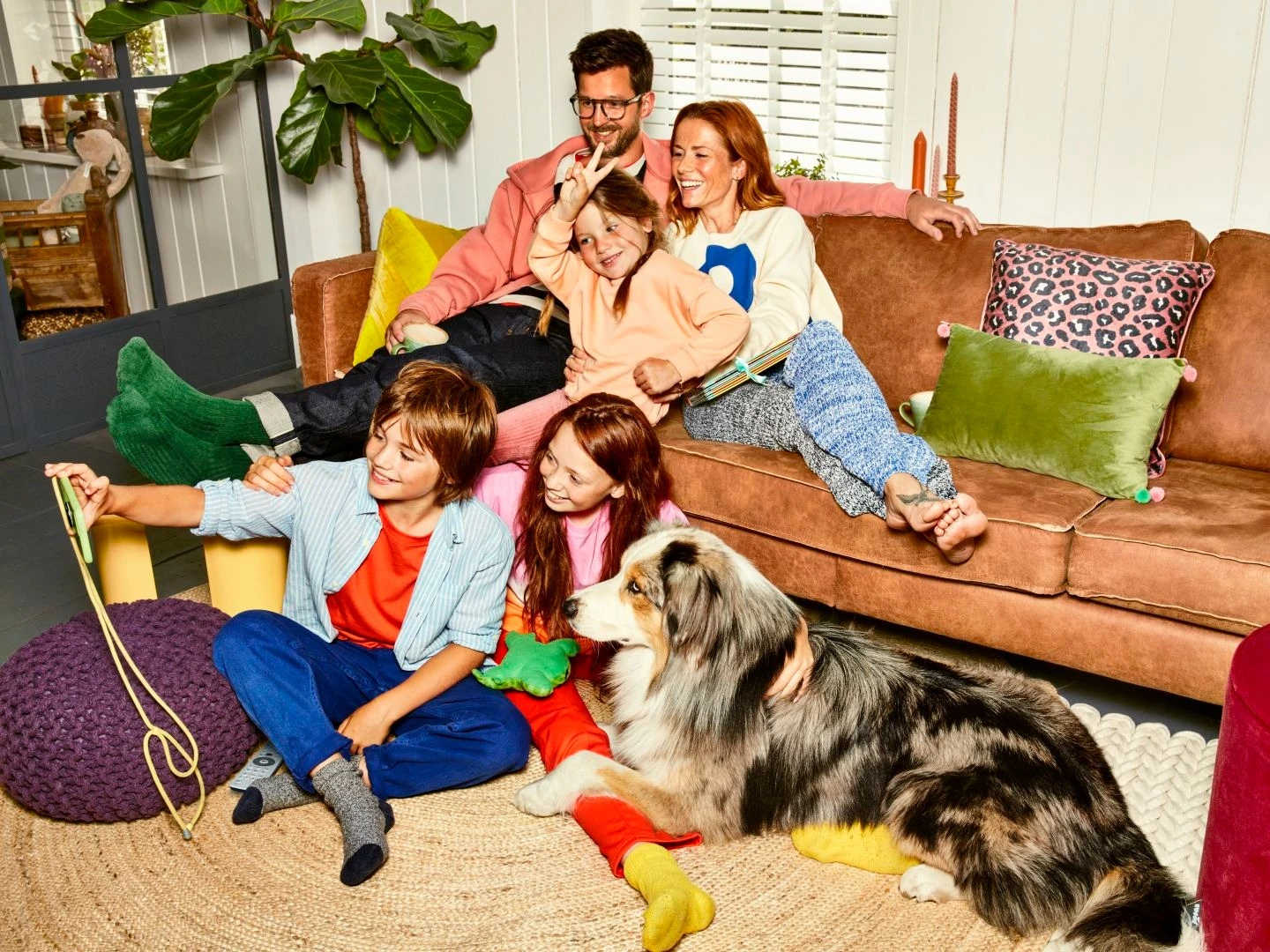 Een gezin van vader, moeder, 3 kinderen en een hond maken selfie op de bank