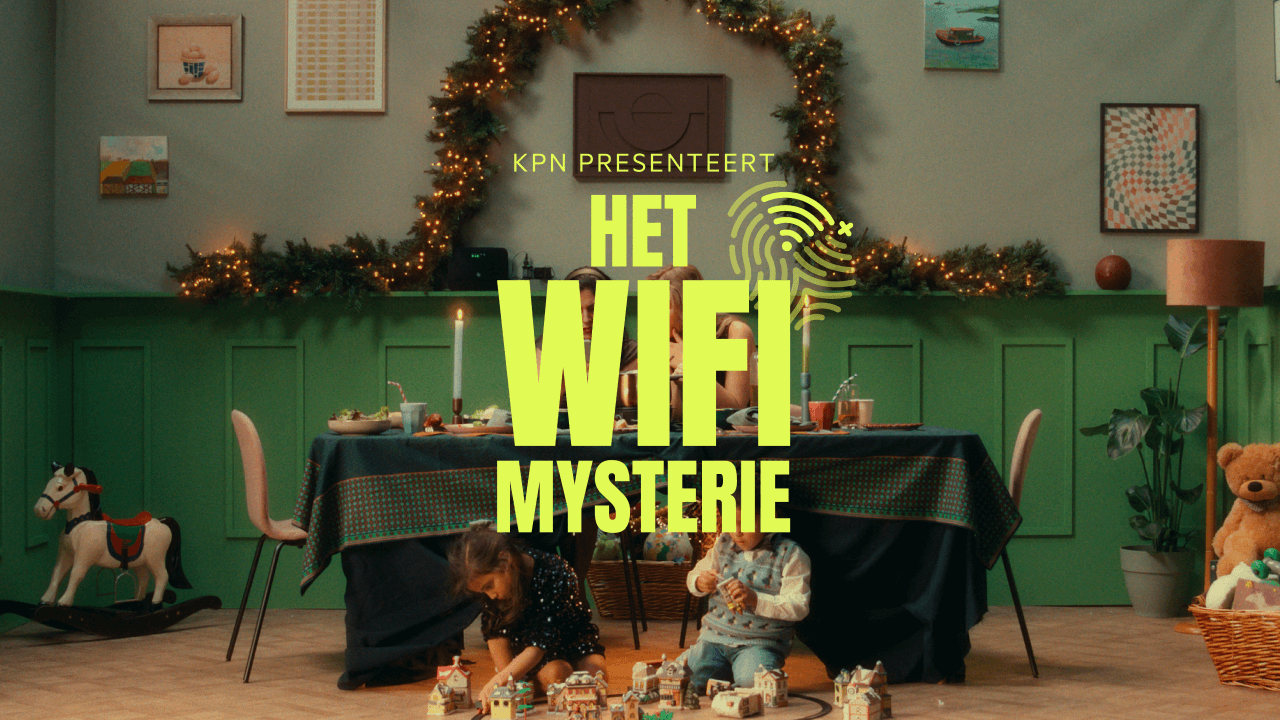 Een gezin zit aan een versierde tafel, de kinderen spelen op de grond voor de tafel. Met op de voorgrond "KPN presenteert het Wifi Mysterie" in gele letters