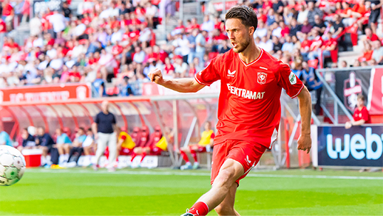 Een voetballer van FC Twente schiet een bal weg in een stadion vol toeschouwers