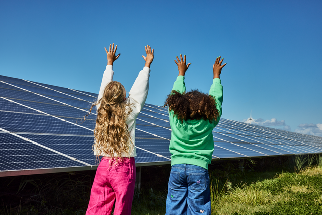 Twee kinderen bij zonnepanelen terwijl ze hun handen in de lucht houden