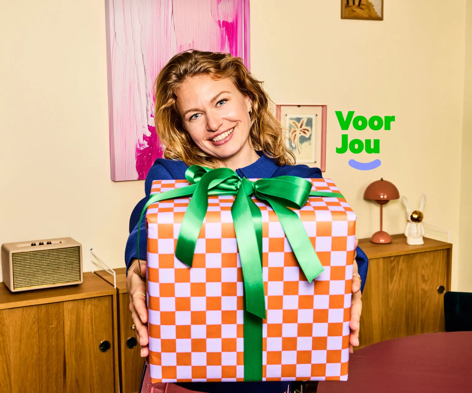 Vrouw met een cadeautje in een huiskamer en het logo Voor Jou