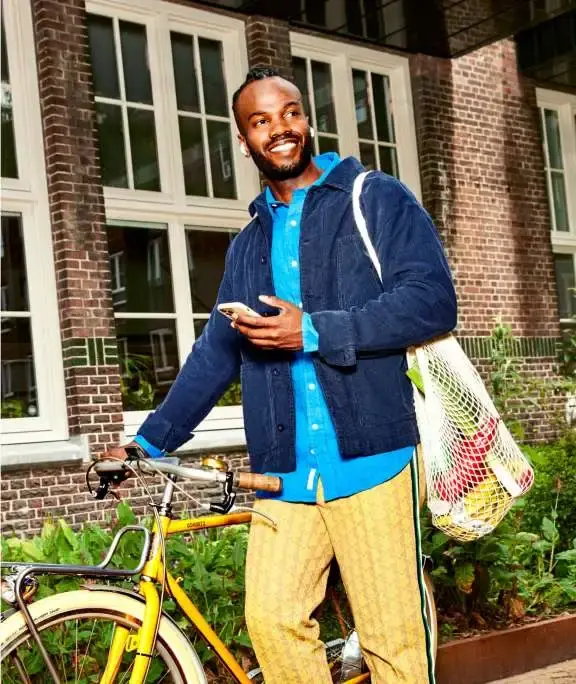 Man lopend met fiets aan de hand en een boodschappentas aan de schouder kijkt op telefoon