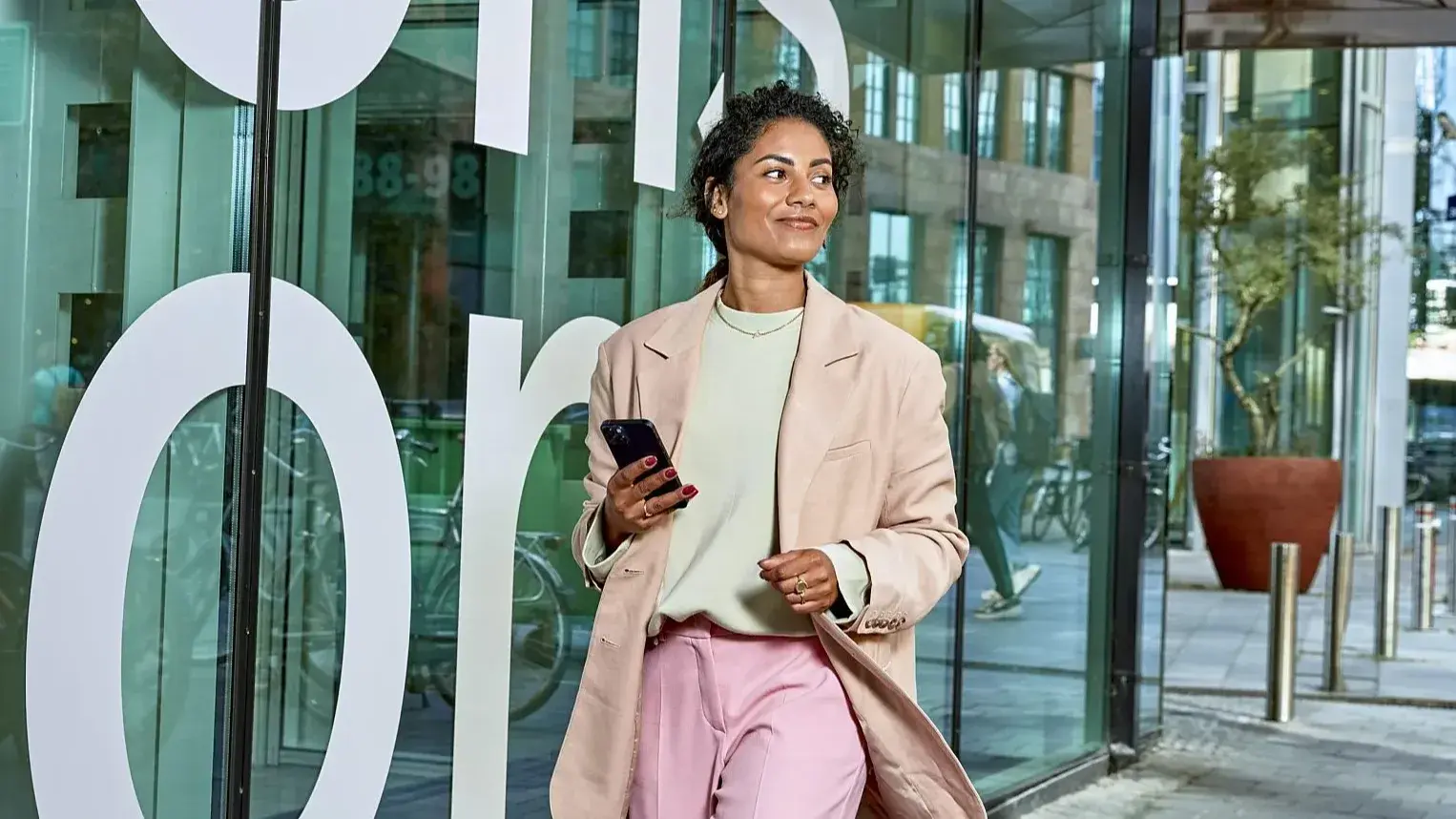 Dame loopt op straat voor het KPN hoofdkantoor met telefoon in de hand