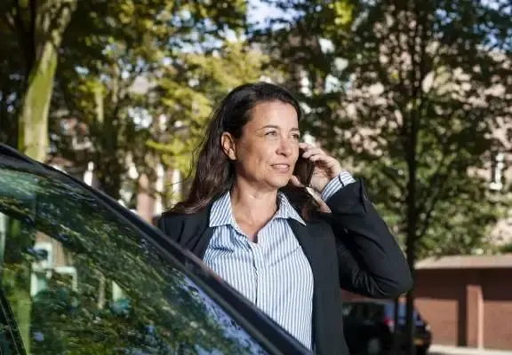 Dame met telefoon aan het oor, staande naast een auto