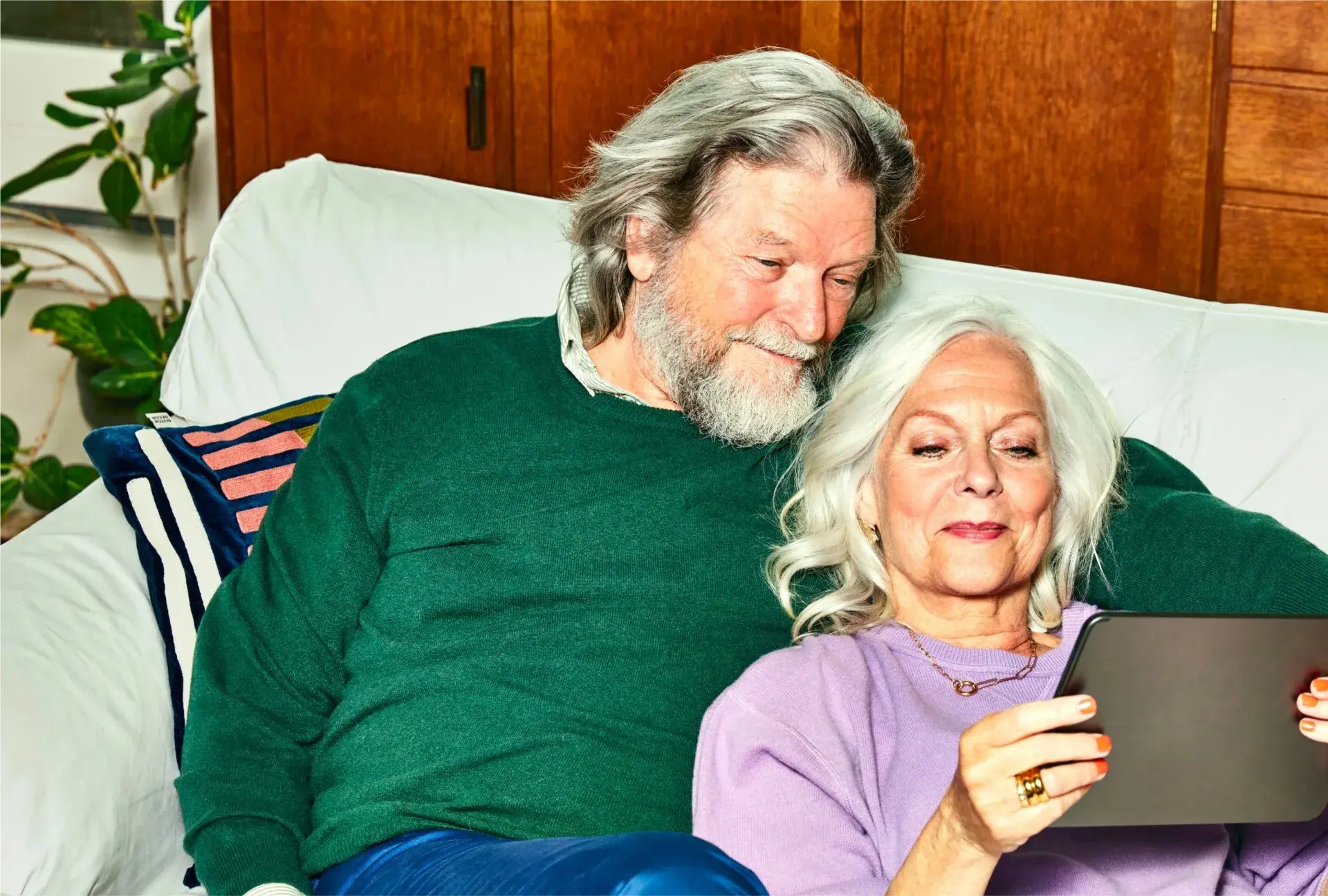 Oudr man en vrouw zitten opde bank en kijken op een tablet