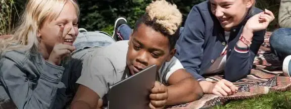 diverse jongelui liggen op een grasveld en kijken naar een tablet