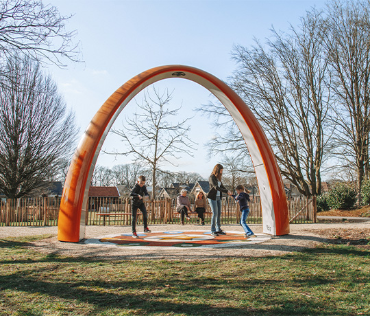 1390 NL Sona De Stroet 2021-884 Family playing under the Lappset Sona Interactive dance and play arch. While two elderly relax on a bench in the background.