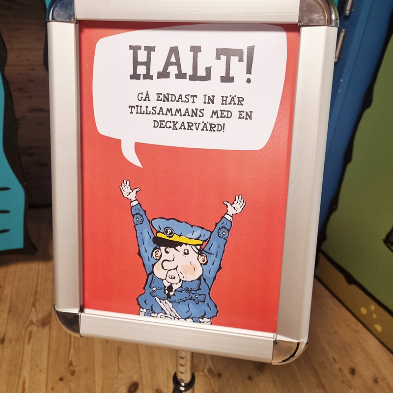 Rio och Aaron LasseMaja 3 800x800 A sign features a cartoon policeman with a stern expression, raising a hand. Text in Swedish reads,