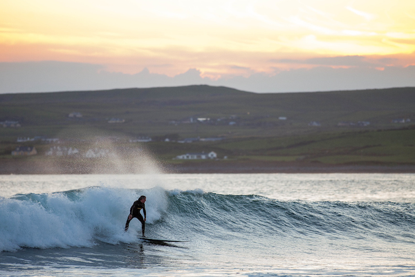 Surfer A surfer rides a wave with a sunset behind him in Ireland