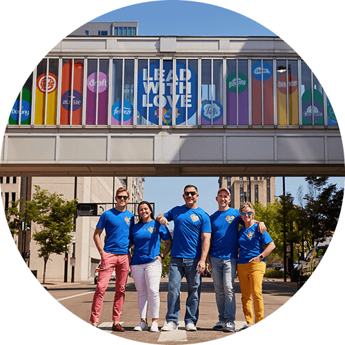 Five members of P&G’s “GABLE employee resource group stand in front of a bridge with a sign that reads, “Lead with Love.”