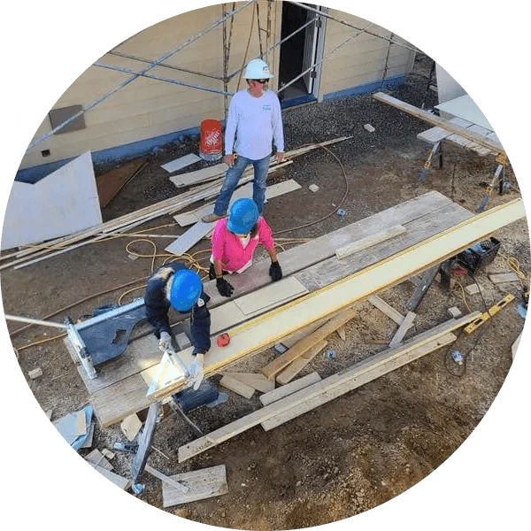 Aerial view of three volunteers cutting boards to build a house.