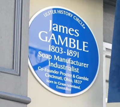 Blue heritage plaque reading “James Gamble 1803–1891, Soap Manufacturer, Industrialist, Co-founder Procter & Gamble” mounted on a building exterior.