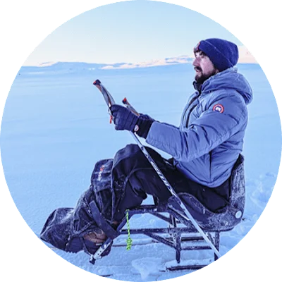 An image of adaptive adventurer, Darren Edwards, as he prepares to sit-ski to the South Pole. He is wearing a thick, warm pale blue coat and woolly hat. He is sitting on a sit-ski, and is against a snowy landscape.