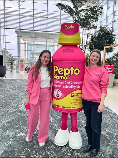 Two smiling women posing for a photo next to the Pepto-Bismol mascot.