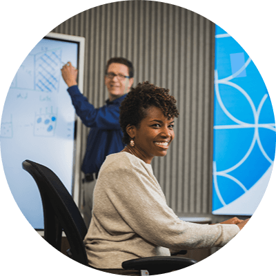 One female and two male P&G employees collaborating in P&G workspace. Female employee and P&G logo are at center of image and male employees are to each side.