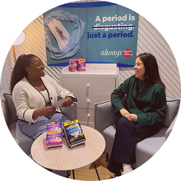 Two women having a conversation with a A period is just a period poster by Always behind them